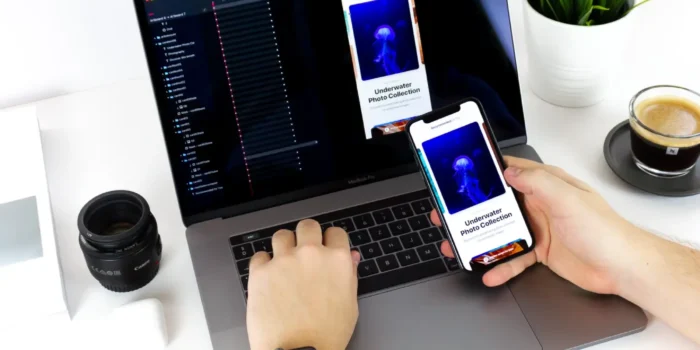 person holding mobile phone in front of a laptop that shares the same screen to signify mobile app development in malaysia.