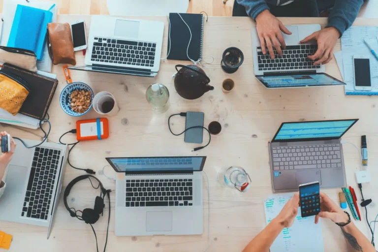 An overhead shot of a shared workstation with people working on laptops signifying in-demand software engineer jobs.